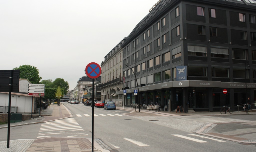 Vi ser Strandgata nordover fra stasjonen med First Hotel Victoria til høyre. Jernbanelinja ligger til venstre parallelt med Strandgata. Det er innkjøring forbudt til hotellet fra denne siden. Dette er Enggata som er enveiskjørt i sentrum. Skal man sette av passasjerer ved hotellet, må man kan kjøre inn i Enggata fra andre enden, f.eks. fra Torggata. Det går også en vei ned til venstre. Dette er en jernbaneundergang som fører over til «sjøsiden» av Hamar. Dette er også veien til Tjuvholmen Kro, en utstikker i Mjøsa med flott oversikt over sentrum fra «sjøsiden».